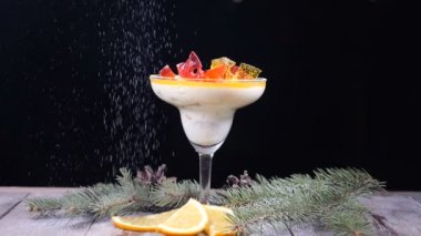 Ahşap tahta üzerinde cam kase lezzetli tatlı köknar-ağaç dalları ve limon dilimleri ile dekore edilmiştir. Siyah arka plan üzerine izole. Tatlı ağır çekimde üzerine pudra şekeri dökme. HD