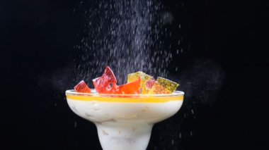 Ahşap tahta üzerinde cam kase lezzetli tatlı köknar-ağaç dalları ve limon dilimleri ile dekore edilmiştir. Siyah arka plan üzerine izole. Tatlı ağır çekimde üzerinde pudra şekeri dökerek.