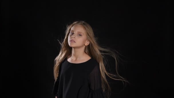 Portrait of little model in studio isolated on black background. Touching her hair in slow motion, looking at camera, posing. hd — Stock Video