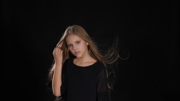 Portrait of little model in studio isolated on black background. Touching her hair in slow motion, looking at camera, posing. hd — Stock Video