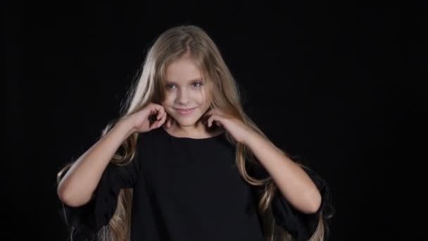 Portrait of little model in studio isolated on black background. Touching her hair in slow motion, looking at camera, posing. hd — Stock Video