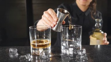 Ağır çekimde viski aletlerden dışarı dökme kadın barmen. Siyah üniformalı tanınmaz halde kadın barmen. HD
