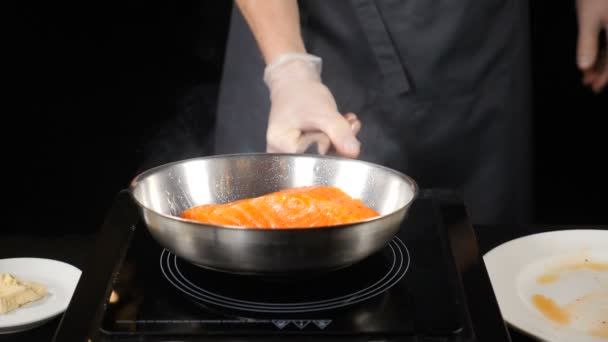 专业厨师在餐厅烹饪。精致的餐饮理念。男性手拿着煎锅与鳟鱼圆角上。慢动作. — 图库视频影像