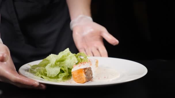 Chef-kok in handschoenen draaien schotel met freshfried Zalm Filet geserveerd met groenten en sla op wit bord. HD — Stockvideo