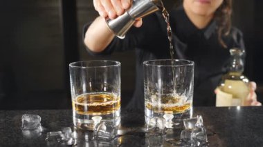 Ağır çekimde viski aletlerden dışarı dökme kadın barmen. Siyah tişörtlü tanınmaz halde kadın barmen. HD