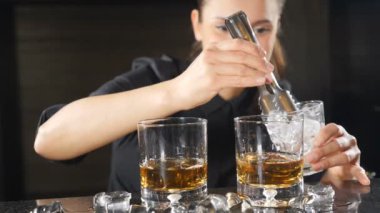 Ağır çekimde alkollü içecek içine koyarak buz kadın barmen closeup çekim. kokteyller ruhu ile siyah üniformalı barmen tarafından hazırlanır. HD