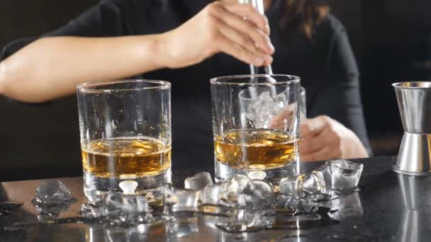 Cantinera arrojando cubitos de hielo en un vaso con whisky en cámara lenta. Hielo cayendo salpicando. Barman joven preparando cócteles alcohólicos. Hd — Vídeos de Stock