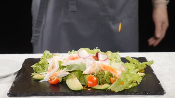 Hälsosam mat och vegetariska konceptet. Kocken hälla sås på sallad med grönsaker placeras på svart sten tallrik. Slow motion. HD — Stockvideo
