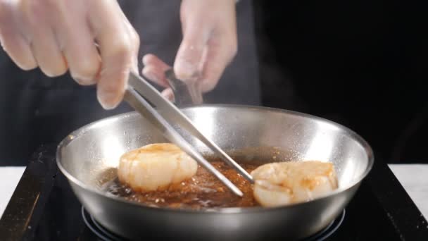 Cocinar mariscos. concepto de comida saludable. Chef profesional en guantes cocinando vieiras convirtiéndolas con alicates culinarios en cámara lenta. hd — Vídeo de stock