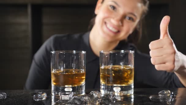 バーとカクテルのコンセプト。ウイスキーに近いカクテルを黒制服示す親指で女性バーテンダー。成功のコンセプトです。スローモーション。メガネ フォーカスされます。hd — ストック動画