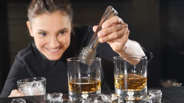 Nachtleven in een club. Vrouwelijke barman alcoholische cocktails in wijnglazen blokjes ijs aanbrengend slowmotion voorbereiden. Ijs is vallen met spatten. HD — Stockvideo