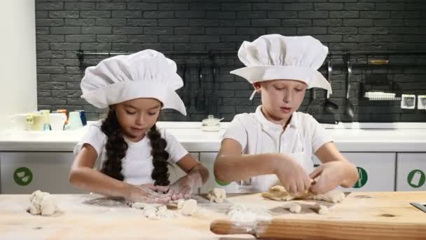 Två förskola barn arbetar sida vid sida matlagning pajer och kakor. Barn kockar bär hattar och förkläden. 6-7 år gamla killar spela kockar. 4k — Stockvideo