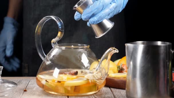 Préparation de thé chaud avec de l'alcool. Verser du vin rouge chaud dans une théière en verre avec des fruits biologiques. Au ralenti. Barman en gants. hd — Video