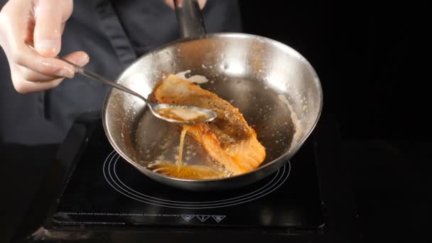 Concepto de comida. Salmón frito, trucha. Piel de filete de salmón boca abajo en la sartén. Trozos de pescado rojo fritos en una sartén. Chef vertiendo aceite con una cuchara. hd. Movimiento lento . — Vídeo de stock