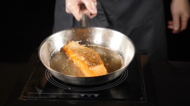 Concetto di ristorazione. Salmone fritto in padella, trota. Filetto di salmone a testa in giù sulla padella. Fette di pesce rosso fritte in una padella. Chef versare olio con un cucchiaio. hd. Rallentatore . — Video Stock