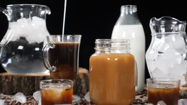 Σύνολο των φιαλών που γεμίζουν με νερό και γάλα στα παρασκήνια με ένα ποτήρι σκούρο καφέ στη μέση. Γάλα μπουμπουνητά αραίωση καφέ σε αργή κίνηση. Καφέ έννοια. HD — Αρχείο Βίντεο