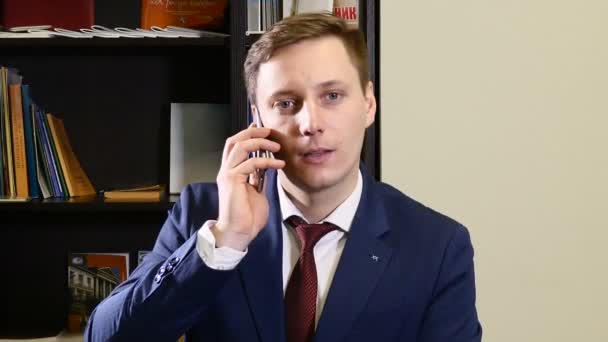電話で話しているオフィスでスーツの若い男は。スマート男は室内での携帯電話を呼び出します。ハンサムな若いビジネス人スマート フォン幸せの身に着けているスーツのジャケットを笑顔で話しています。都市男性のプロ — ストック動画