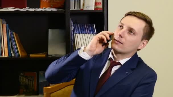 Un joven de traje en la oficina hablando por teléfono. Un hombre inteligente llamando al teléfono móvil interior. Hombre de negocios joven guapo hablando en el teléfono inteligente sonriendo feliz usando chaqueta de traje. Hombre urbano profesional en — Vídeo de stock