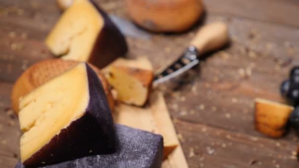 Vídeo de comida. Top vista tiro na vaidade de queijo delicioso duro colocado em tábua de corte de madeira. Restaurante conceito de comida de luxo. Cabeça redonda inteira de queijo duro parmesão ou parmigiano, uvas em madeira — Vídeo de Stock