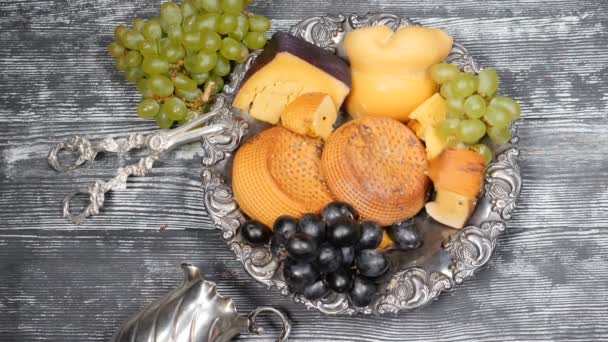 Il concetto di cibo di lusso. Ristorante di formaggi che serve. Concetto di arte alimentare. Varietà di formaggio a pasta dura e ramo d'uva su piatto d'argento di rarità messo su asse di legno. Pezzi di formaggio duro sono gettati in lento — Video Stock