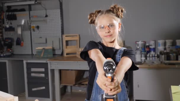 Adorable joven en delantal sosteniendo un taladro en carpintería. Retrato de una niña con un taladro mirando a la cámara. En cámara lenta. hd — Vídeos de Stock