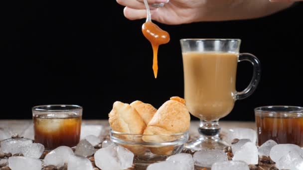 Kaffehus med läckra croissanter på glasskiva. Heta rensa flytande karamell öser ner på dessert i slow motion. Kopp aromatiskt latte på bakgrunden. Isbitar, kaffebönor på träskiva — Stockvideo