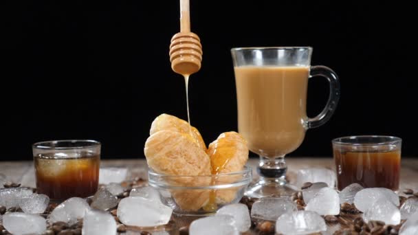 Caffetteria con deliziosi croissant su piatto di vetro. Miele liquido chiaro caldo che si riversa sul dessert al rallentatore. Tazza di latte aromatico sullo sfondo. Cubi di ghiaccio, chicchi di caffè su tavola di legno — Video Stock