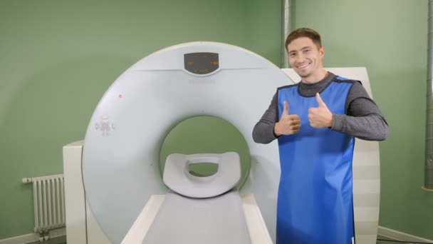 Conceito de tomografia computadorizada. Paciente jovem do sexo masculino, próximo ao tomógrafo. Polegar para cima. Conceito de saúde. Exame de ressonância magnética. hd — Vídeo de Stock