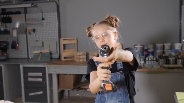 Portrait d'une jeune fille de 10 ans en menuiserie de bois tenant une perceuse électronique, posant à la caméra. Concept de petit constructeur. hd 