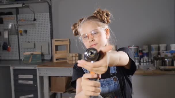 Portrait d'une jeune fille de 10 ans en menuiserie de bois tenant une perceuse électronique, posant à la caméra. Concept de petit constructeur .