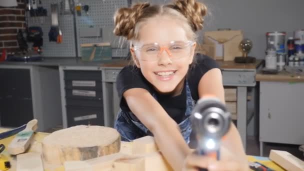 Портрет 10-річної дівчинки в дерев'яній столярній майстерні, що тримає електронну дриль, позує на камеру. Маленька концепція будівельника. hd — стокове відео