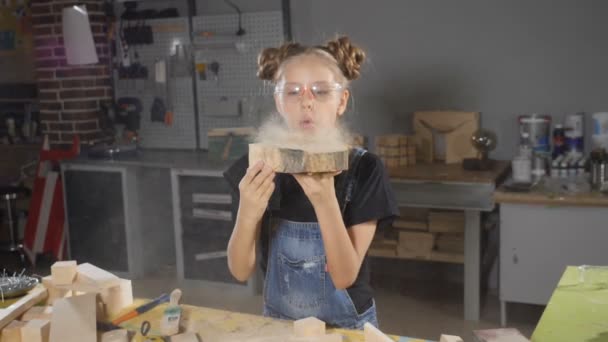 Tourné de fille blonde dans un tablier soufflant de la sciure de bois au ralenti. Des enfants en menuiserie. Hd 