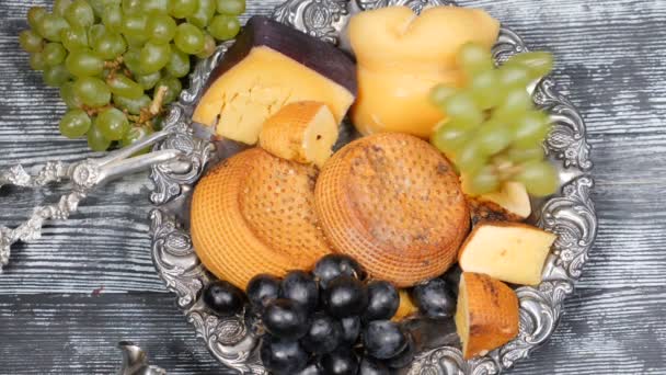 Luxury food concept. Cheese restaurant serving. Food art concept. Variety of hard cheese and branch of grapes on rarity silver plate put on wooden board. Top view shot. Slow motion. hd — Stock Video