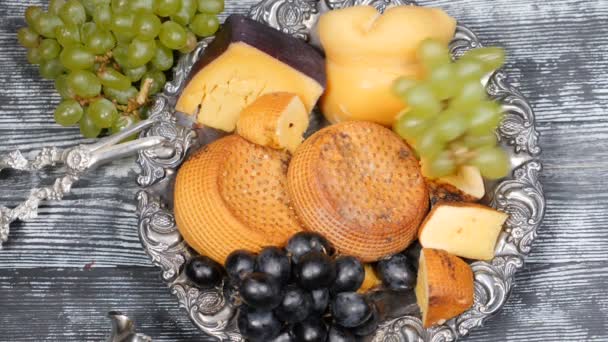 Concepto de comida de lujo. Servicio de restaurante de queso. Concepto de arte alimenticio. Variedad de queso duro y rama de uva en plato de plata rareza poner en tablero de madera. Vista superior. En cámara lenta. hd — Vídeo de stock