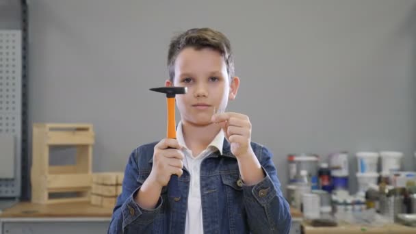 Garçon et le bâtiment met en œuvre avec Marteau et les ongles dans les mains fermer et ouvrir les yeux souriant. Concept artisanal. hobby et temps libre à l'atelier serruriers .