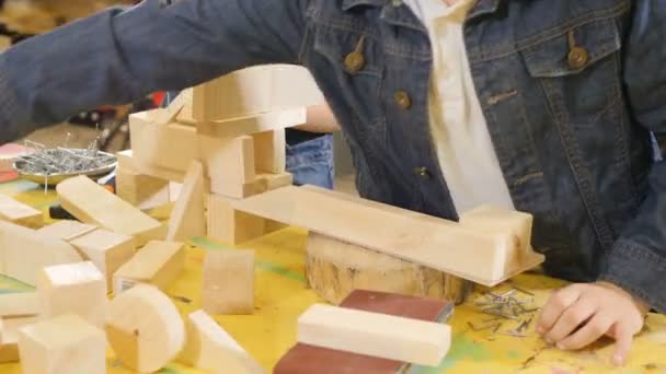 Los niños juegan en el taller de artesanía. Lindo niño jugando con trozos de madera. Primer plano disparado. Edificio de chicos. 4k — Vídeos de Stock