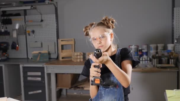 Portrait of 10 year old girl in wood carpentry holding an electronic drill, posing at camera. Little builder concept. hd — Stock Video