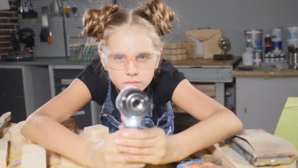 Retrato de engraçado menina de 10 anos de idade em carpintaria de madeira segurando uma broca eletrônica, posando para a câmera. Um pequeno conceito de construtor. hd — Vídeo de Stock