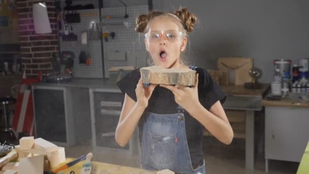 Tourné de fille blonde dans un tablier soufflant de la sciure de bois au ralenti. Des enfants en menuiserie. Hd 