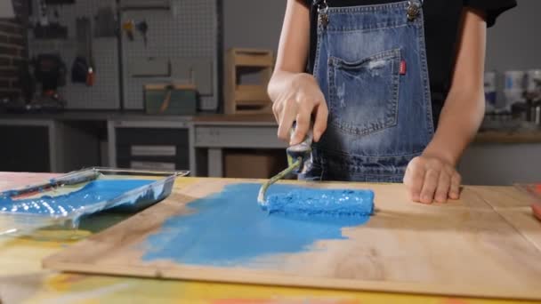 Primer plano de una niña pintando de azul. Tablero de pintura con rodillo. De cerca. En cámara lenta. hd — Vídeos de Stock