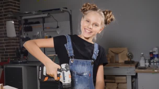 Little 10 year-old girl and a drill in hands. Slow motion. Young pretty girl builder is holding drill in her hands, turning on, smiling, building conception. hd — Stock Video