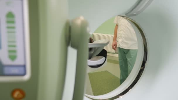 Βολή closeup της αρσενικός ασθενής κινείται σε έναν σαρωτή Ct. Ιατρικός εξοπλισμός: μηχανή τομογραφία υπολογιστών στην σύγχρονη κλινική. Έννοια της υγείας. Γιατρός πιέζει το κουμπί ρυθμίσεις αξονική τομογραφία σαρωτή. HD — Αρχείο Βίντεο