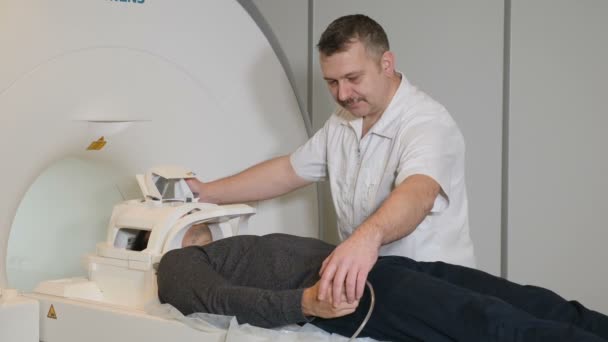 Концепция компьютерной томографии. Концепция здоровья. Мужчина сканируется магнитно-резонансным томографом в современной больнице. Врач-рентгенолог в белом халате готовит пациента к КТ — стоковое видео