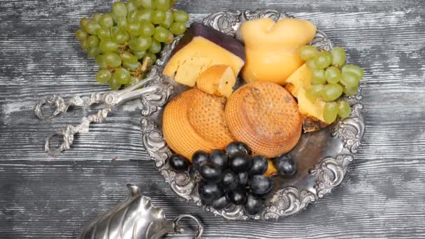 Conceito de comida de luxo. Restaurante de queijo a servir. Conceito de arte alimentar. Variedade de queijo duro e ramo de uvas na chapa de prata raridade posta na tábua de madeira. Pedaços de queijo duro são jogados em lento — Vídeo de Stock