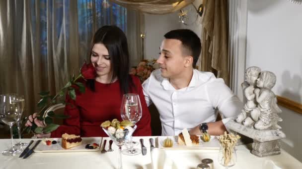 Romantische relaties concept. Paar dating in restaurant. roos in handen, romantische datum. 14 februari-concept. Vrouw in het rood houden van een bloem. HD — Stockvideo