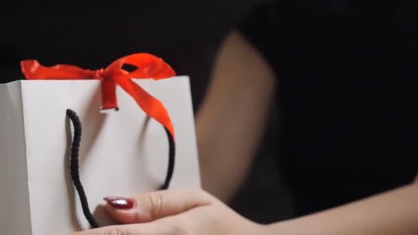 Parmaklar gösterir kağıt hediye kutusu kırmızı kurdele ve bir yay ile kapatın. hediye kutusu kadın olarak tutan bir hediye açılış yay-knot siyah bir zemin üzerine bağcıklı. HD — Stok video