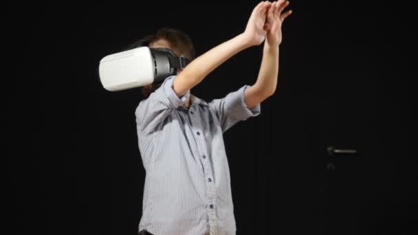 Concepto científico futuro. Concepto infantil contemporáneo. Niño utilizando dispositivo de realidad virtual en el estudio con negro blackground. Un chico con gafas VR. Primer plano disparado. El chico mira emocionalmente a su alrededor. Lejos. — Vídeo de stock