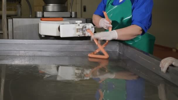 Producción de salchichas en la fábrica de procesamiento de carne. Fábrica de alimentos. Trabajadores de fábricas de salchichas produciendo salchichas. Línea automática en planta cárnica. Manos de trabajadores formando salchichas y salchichas colgantes para ser — Vídeo de stock