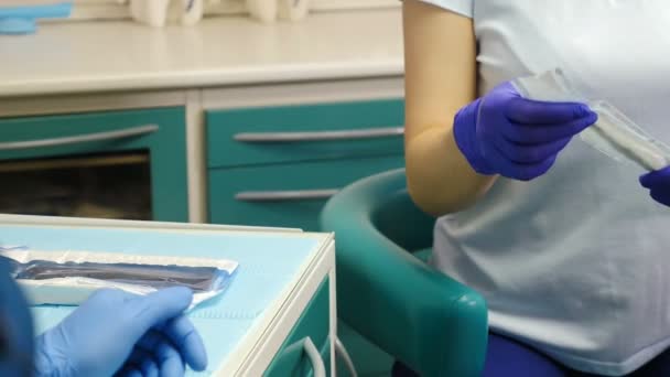 Tandläkare kontor. Tand-behandling. Närbild skott för kvinnliga tandläkare assistant i handskar öppna paketet med steril spegel och scaler verktyg och ger det till läkare. Förberedelse för läkarundersökning — Stockvideo
