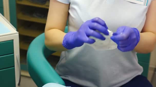Tratamiento dental. Primer plano de la asistente dentista femenina en el paquete de apertura de guantes con expansor de boca estéril. Preparación para el examen médico. dentista en su oficina prepara expansor para la boca — Vídeos de Stock